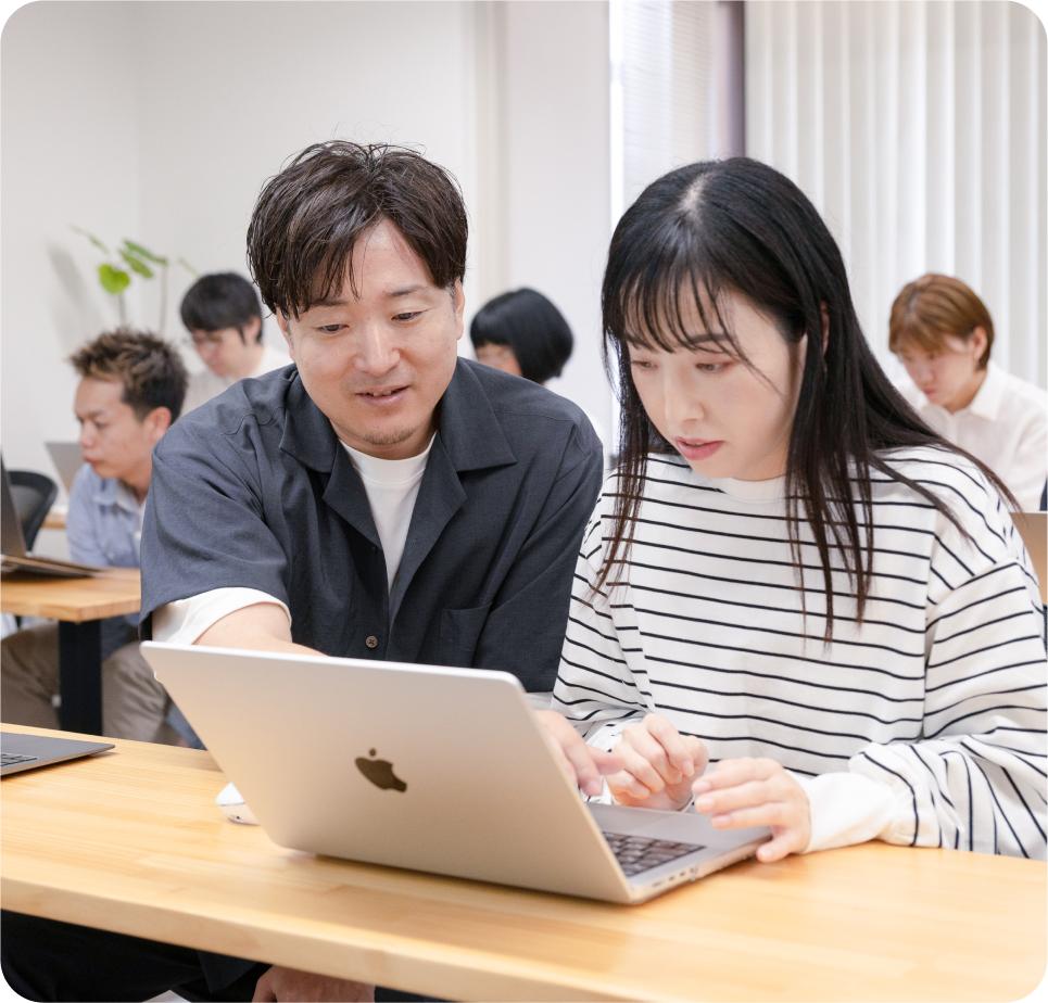 講師が受講者の隣でパソコンを見ながら教える様子